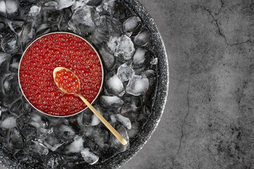 Red caviar in can on ice with spoon on grey background