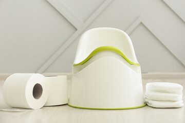 Potty, toilet paper rolls and diapers on light wooden floor near wall