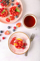 Plates with tasty berry tartlets and cup of tea on light background