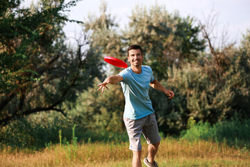 Young man throwing frisbee in park - obrazy, fototapety, plakaty