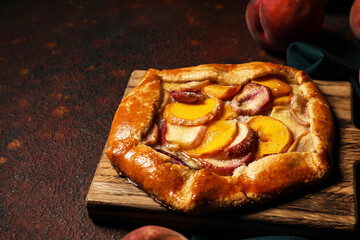 Board with tasty peach galette on grunge background, closeup