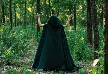 Young witch in green forest, back view
