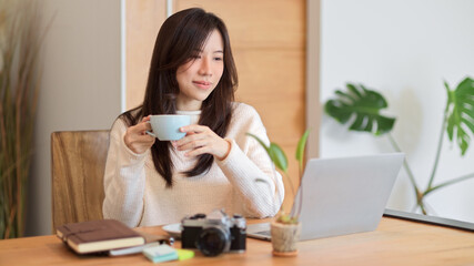 Pleased and cheerful woman drinking morning coffee, relaxation, working on laptop computer