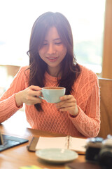 Beautiful young asian female in pink sweater enjoying her afternoon tea at cafe