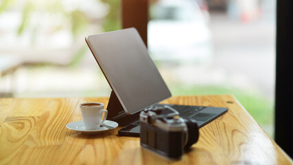 Modern tablet computer stand on wooden table with camera and coffee cup