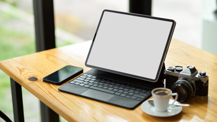 Modern digital tablet computer blank screen mockup with smartphone, camera and coffee cup on table.