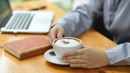 Businesswoman holding hot cappuccino white coffee cup, drinking coffee during works.