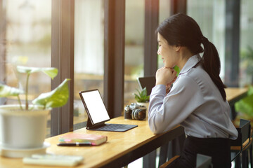 Obraz premium Beautiful young asian businesswoman working on tablet, looking on screen