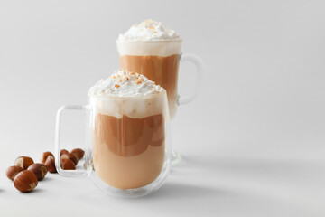 Glass cups of tasty latte with nuts on light background - obrazy, fototapety, plakaty