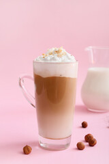 Glass cup of tasty latte with nuts on pink background