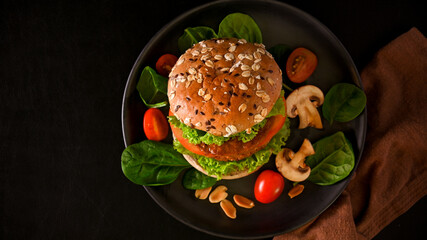 Vegan burger with whole grain bun, vegan meat and fresh organic vegetables on black background.