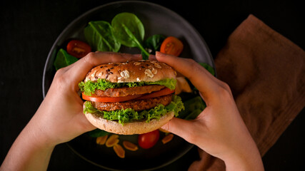 Close-up hands holding tasty vegan burger, soy protein burger with fresh vegetables - obrazy, fototapety, plakaty