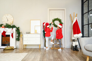 Cute little children hanging wreath on door at home on Christmas eve