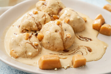 Plate of tasty caramel ice cream with nuts on table, closeup