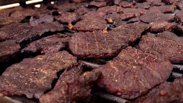 Home cooking - Close up of slices of smoked and dehydrated meat or beef jerky cooling down on grill