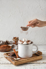 Woman sprinkling cacao powder into mug with tasty hot chocolate on table