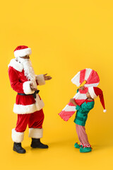 Cute little elf with candy cane pinata and Santa Claus on yellow background