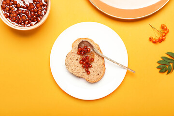 Plate with piece of bread and rowan jam on color background, closeup