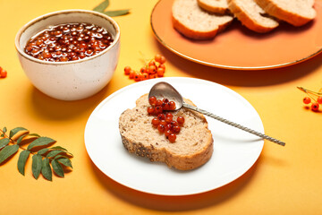 Plate with piece of bread and rowan jam on color background, closeup