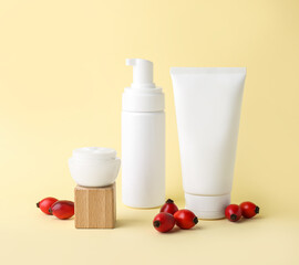 Different cosmetic products and rose hip berries on color background