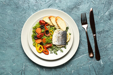 Plate of tasty sea bass fish with vegetables on blue background