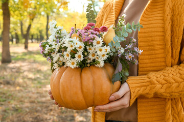 Woman holding beautiful bouquet of autumn flowers in pumpkin outdoors