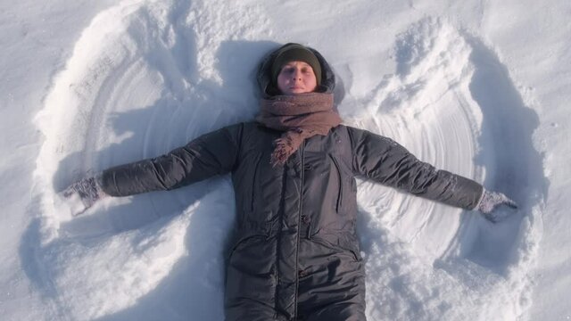 Young woman lying on the snow and painting a snow angel by hands. 