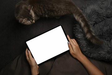 Young woman sitting on bed with her cat and using digital tablet.