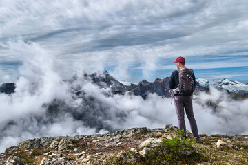 Sporty man hiker standing on cliff above mountains and clouds looking at view from above. Garibaldi...