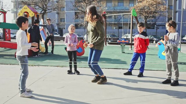 Energetic kids playing and skipping on elastic jumping rope in european yard
