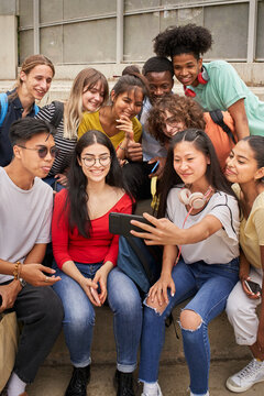 Vertical photo of a group of multi-ethnic students taking selfies with mobile phone. Teenagers using a smart phone and having fun together.