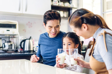 Portrait of enjoy happy love asian family father and mother with little asian girl smiling and having protein breakfast drinking and hold glasses of milk at table in kitchen