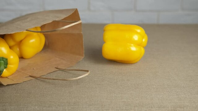 Grocery shopping and vegatables. A female hands takes yellow pappers from the paper bag on the table.