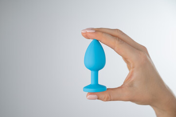 Woman holding a blue anal plug on a white background. Adult toy for alternative sex