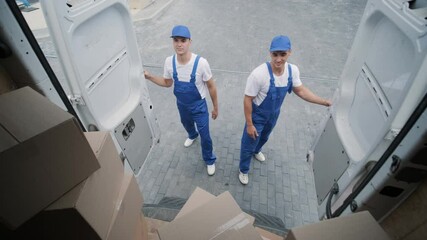 Two young workers of removal company unload boxes and furniture from minibus into customer's home
