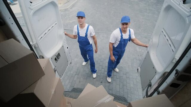 Two young workers of removal company unload boxes and furniture from minibus into customer's home - Powered by Adobe