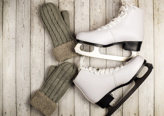 White figure skates and warm woolen mittens on a wooden background. Winter sport and recreation...