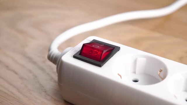 Finger pressing the red button switch of the white electric power strip. Close up. Electricity supply concept. Switching on a extension cord on a wooden background