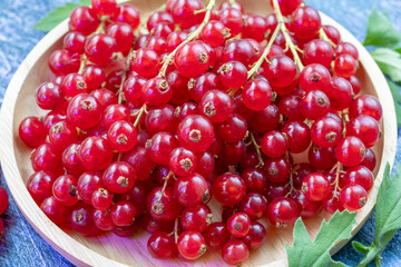 Table top view bunch of red currant in wooden plate, Red currant berries with leaf on a blue wooden table.