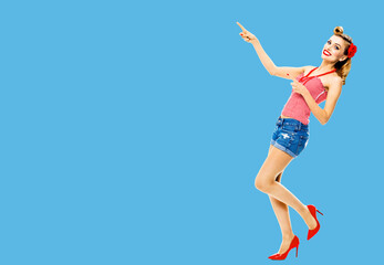 Obraz na płótnie Canvas Full body photo of happy excited smiling woman pointing at something. Blond girl in pin up style, showing copy space area for text or imaginary. Retro fashion and vintage. Blue color background.