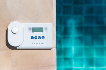 Digital water tester equipment on swimming pool edge with space on blue water background, summer...