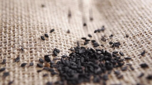 Black sesame seeds falling in a heap in slow motion on a rough rustic burlap. Macro shot. Seasoning ingredient