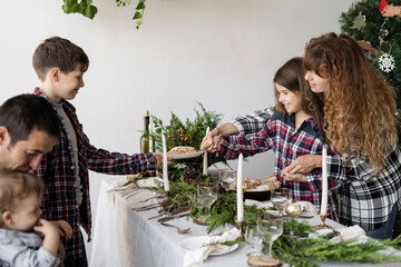 A large family with three children at the Christmas table. Sister gives brother a piece of pie on a plate. Decorated x-mas table in the living room.