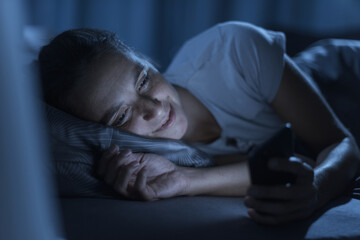 Woman lying in bed at night and connecting with her phone