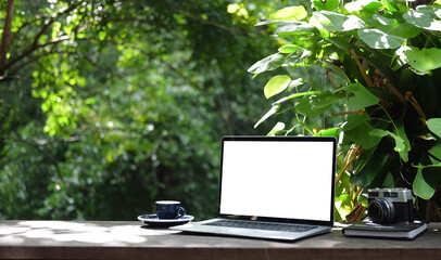 Laptop computer with white blank screen on wooden table in the garden.