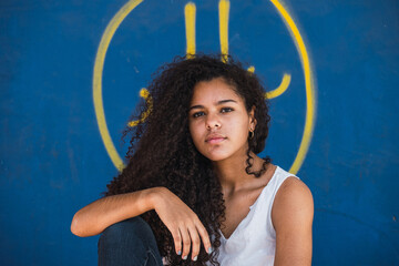 Portrait of a Cuban teenage girl sitting in front of blue wall, closeup teenager woman cuban hispanic