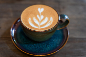 A cup of coffee latte art in blue-green glazed ceramic cup on the wooden table in coffee shop vintage style.