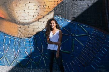 Portrait of a teenage Cuban girl outside in front of a mural with sunlight and, hispanic multiracial teenage woman