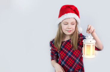 A girl in a Santa Claus hat with a Christmas lantern on a white background. She's Caucasian. A white flashlight in his hands. Christmas. Copy space.