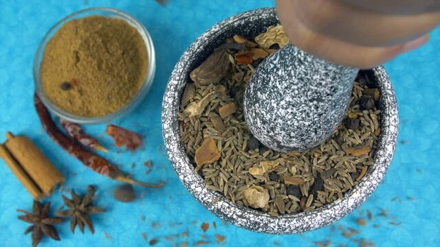 Crushing mixed Indian spices in a mortar pestle - Khade masala from Indian kitchen. Cinnamon sticks  whole dried red chilies  and star anise kept together in a kitchen counter - cooking ingredients
